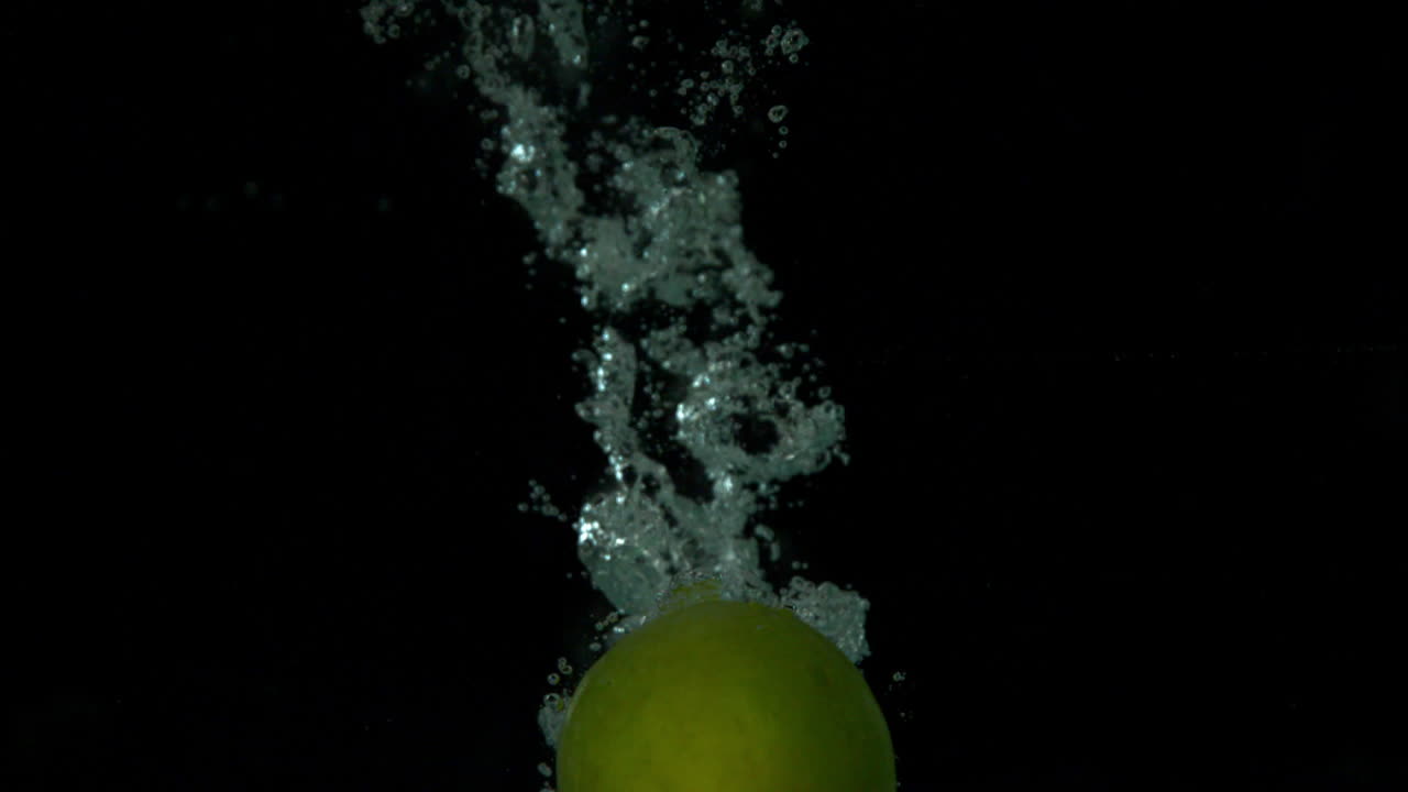 Green apple plunging into water on black background