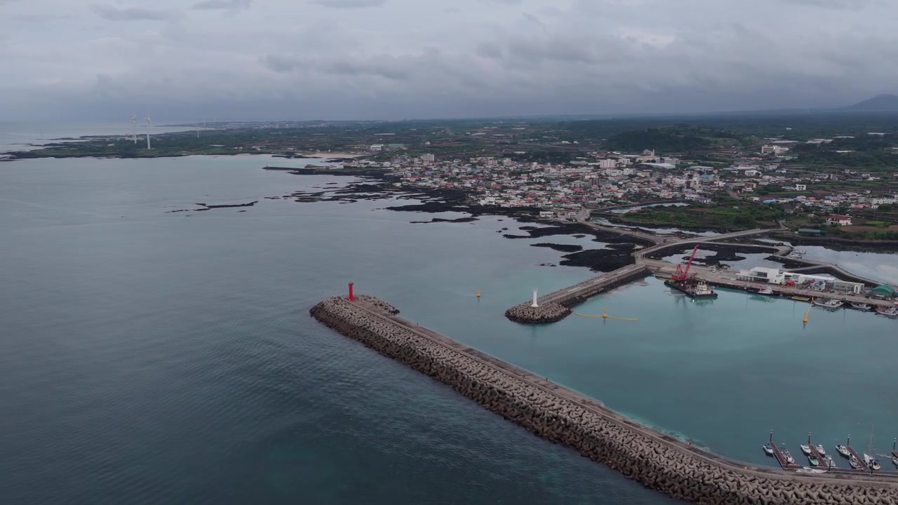 Horizontal cameo shot dollying forward to the right with slight panning left over Gimnyeong Beach, Jeju Island, South Korea, showing harbor breakwaters, ocean, village and volcanic rocks