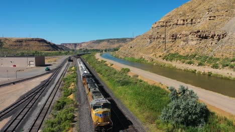 Vista-Aérea-Siguiendo-Un-Tren-En-El-Ferrocarril-Union-Pacific,-Día-Soleado-En-Estados-Unidos