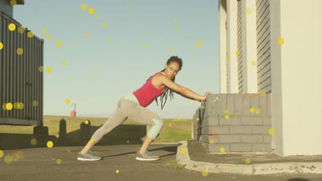 Multiple-yellow-spots-floating-against-african-american-fit-woman-performing-stretching-exercise