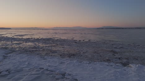 Vista-De-Drones-Del-Horizonte-Coloreada-Con-Los-Colores-Del-Atardecer-Sobre-Un-Lago-Congelado-En-Alaska