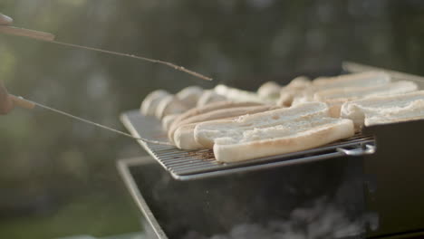 man turning over bread for hotdogs on barbecue grill