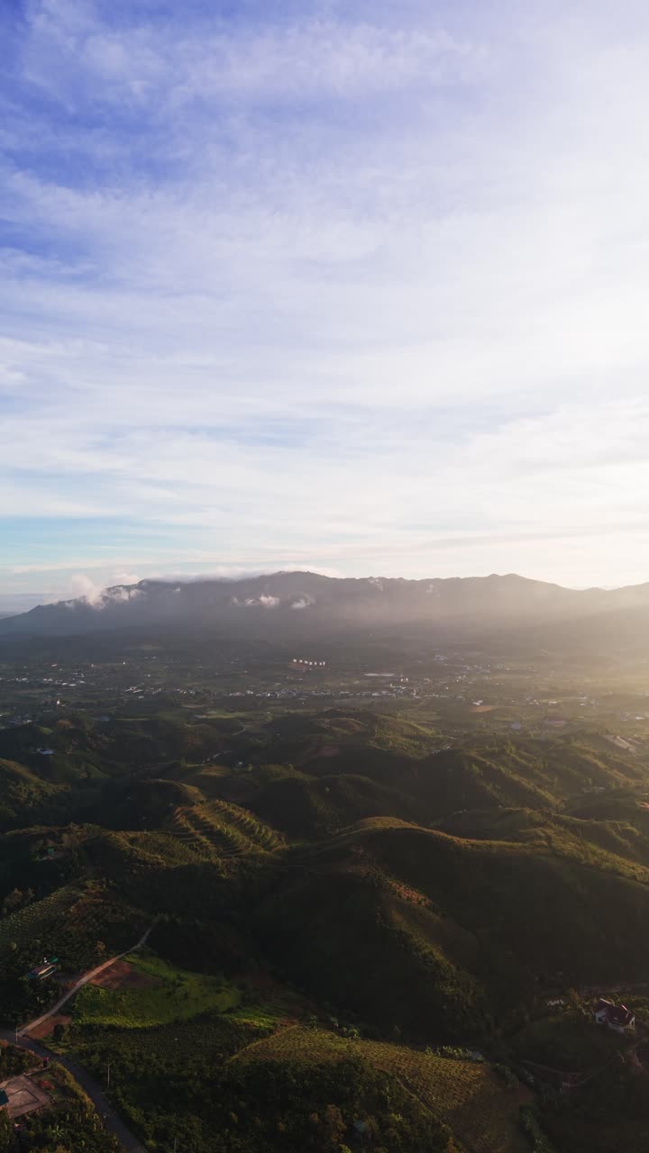 Testemunhe a luz da manhã a romper sobre as colinas e vales de Lam Dong, Vietnã. A paisagem se revela com colinas verdes e montanhas distantes sob um céu claro.