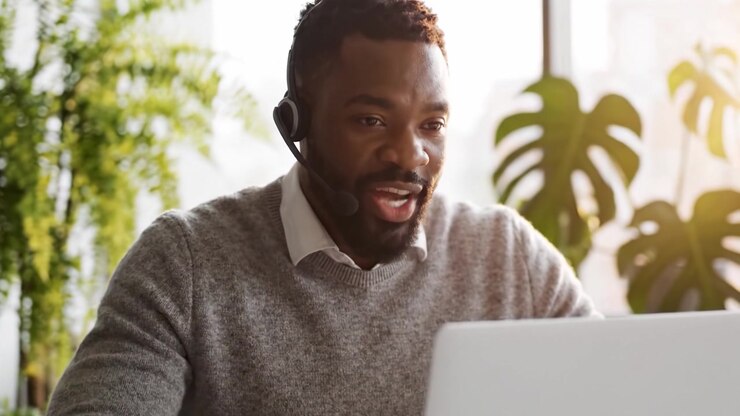 Fokuseret professionel bruger headset og bærbar computer, mens vedkommende arbejder eksternt i et lyst, grønt indendørs rum og deltager i virtuel kommunikation eller et møde.