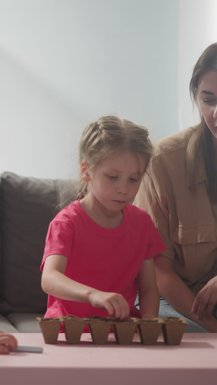 young woman watches how children plant seeds of home plants in small peat pots with soil, home gardening in bright room