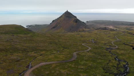 Aerial, reverse, drone shot away from a hill and the ocean, on a cloudy day, in Snaefellsnes peninsula, in west Iceland