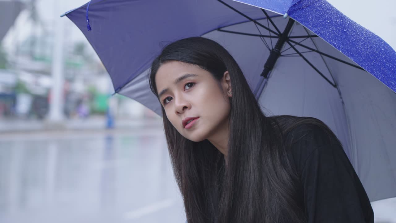 아름다운 동아시아 여성이 도로 에서 혼자 서서 택시나 버스를 기다리고 있다. 비가 내리고, 우산을 들고, 비가 내리는 시간, 급행, 열대 기후 변화, 비가 오는 시기의 도시 스타일.