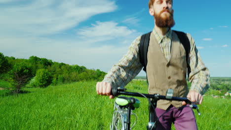 un joven hipster camina con una bicicleta sobre un prado verde