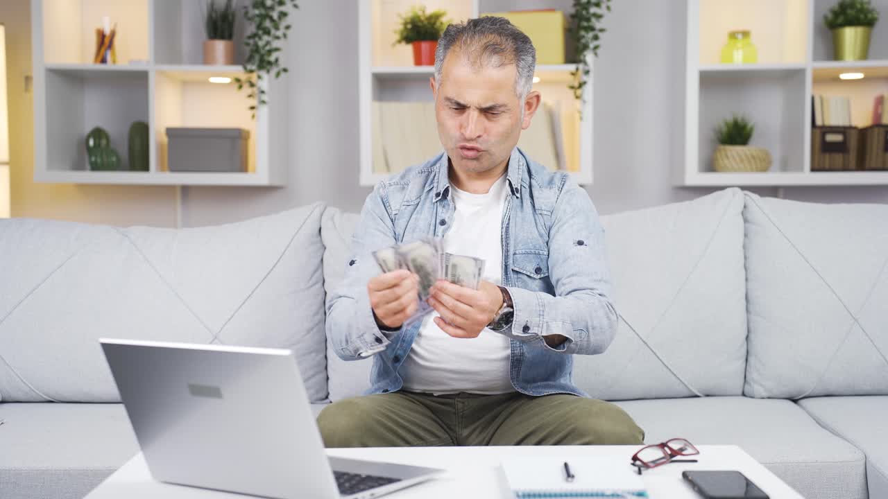hombre mirando la computadora portátil contando dinero.