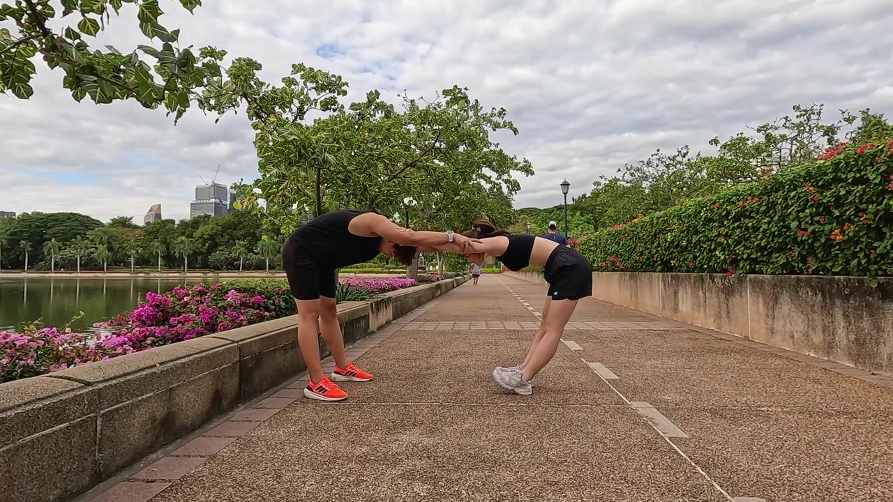Uomo e donna eseguono stretching di coppia su un sentiero del parco vicino al lago sotto un cielo nuvoloso