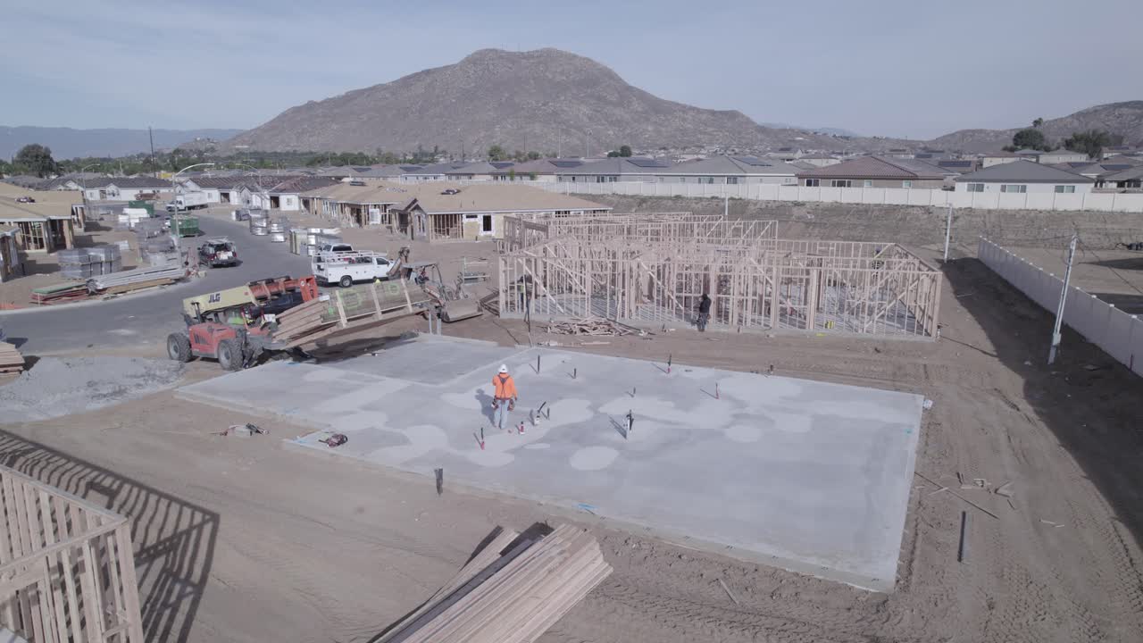 un avión no tripulado observa un montacargas extensible que baja suavemente una caja de madera sobre una base de cemento en un nuevo sitio de construcción de vecindario