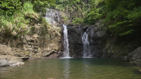 wide slow motion shot of a small, multi-layered waterfalls in the middle of a forest