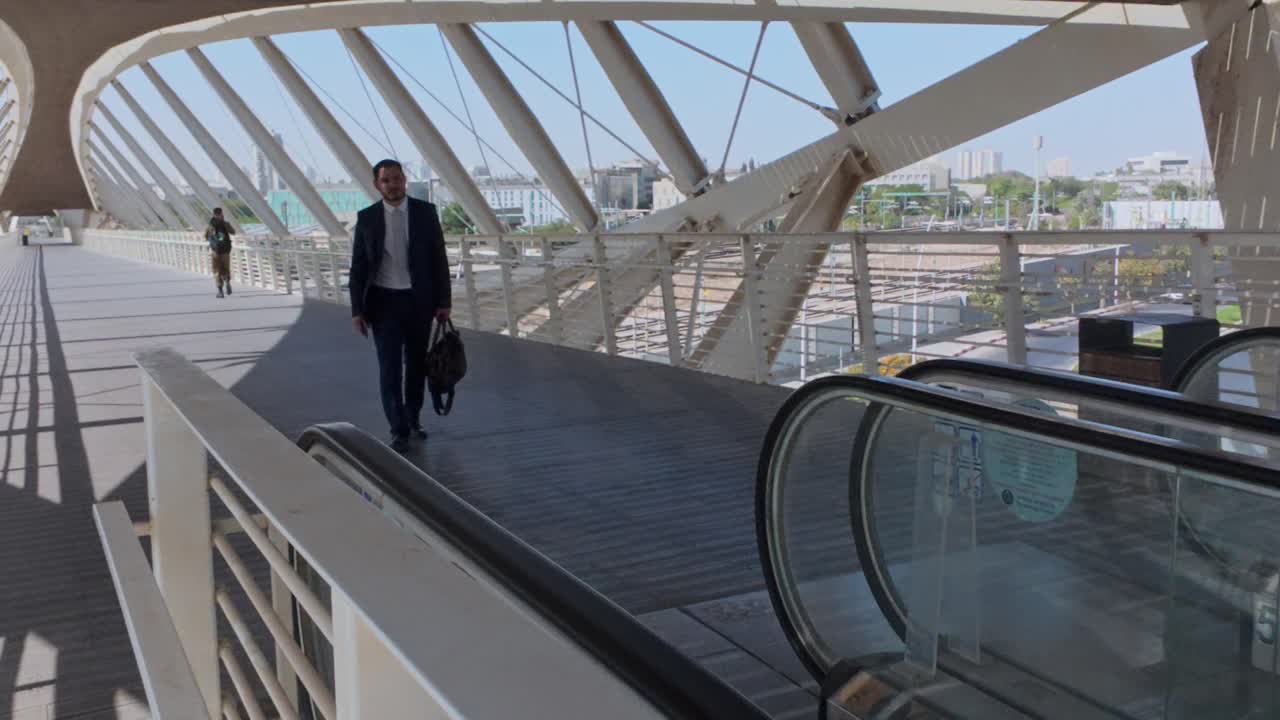 A businessman walks across a bridge with escalators in an urban environment