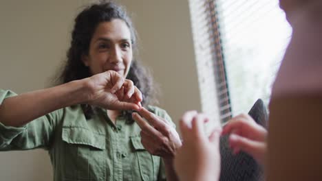 Happy-mixed-race-mother-and-daughter-playing-with-hands-in-living-room