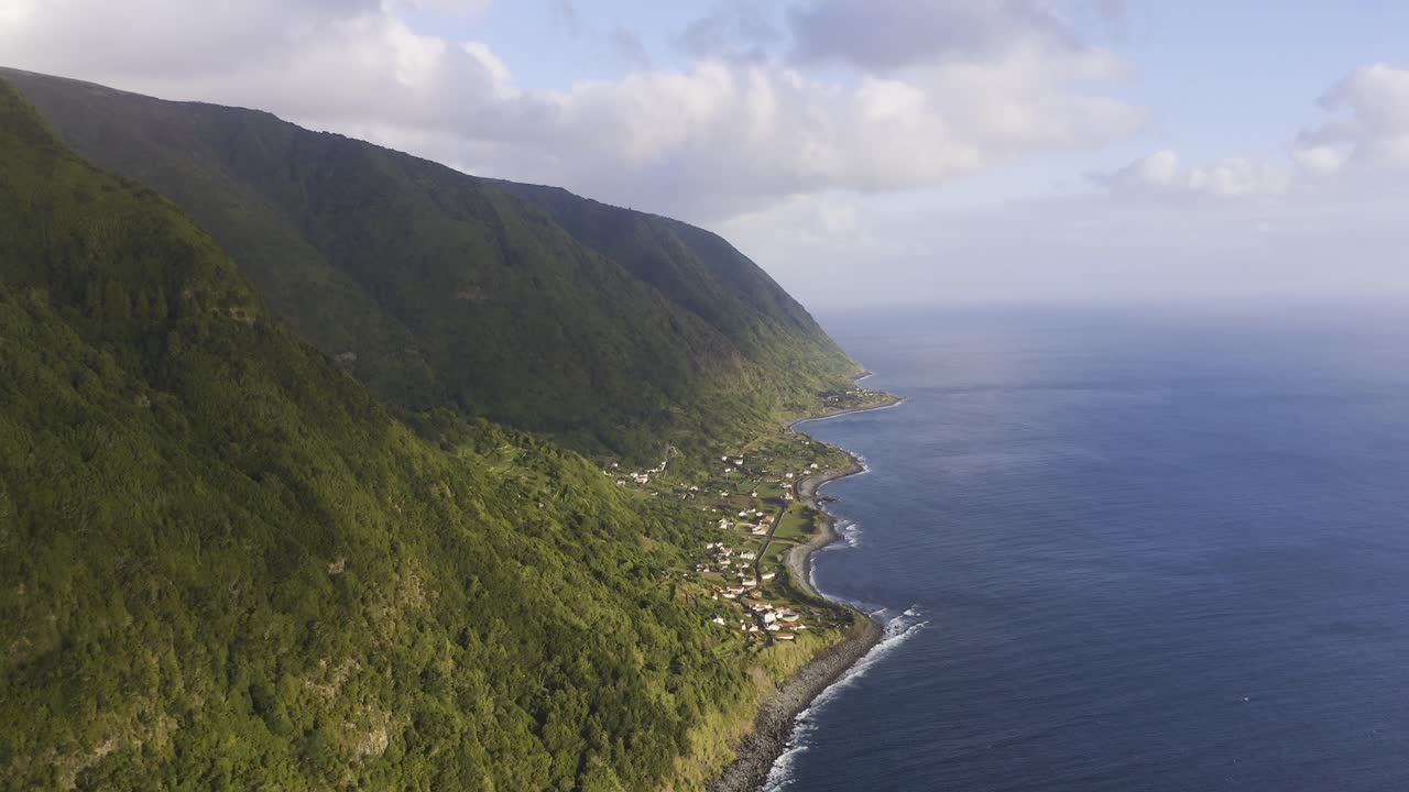 acantilados verdes exuberantes sobre el océano atlántico con un pueblo costero rural, isla de são jorge, las azores, portugal