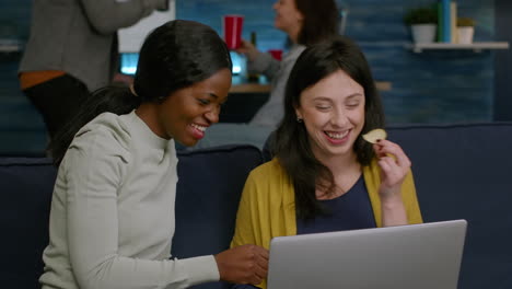 Multi-ethnic-friends-eating-snacks-while-relaxing-on-couch-watching-at-comedy-video