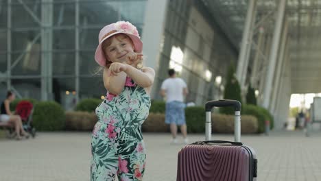 child girl tourist with suitcase bag near airport. kid dances, rejoices, celebrates with luggage