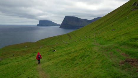 Woman-descending-green-mountain-after-hiking,-Faroe-Islands