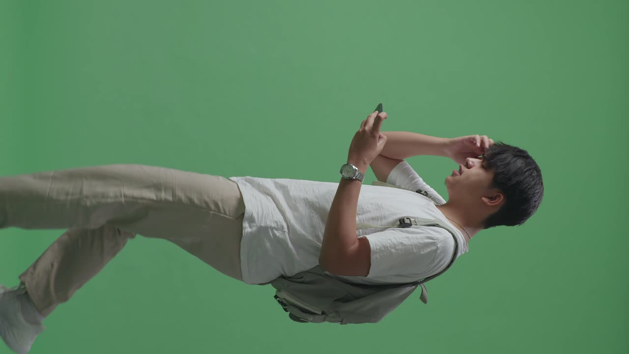 vista lateral de un estudiante asiático enojado jugando a un juego móvil y perdiendo mientras caminaba en el estudio de pantalla verde