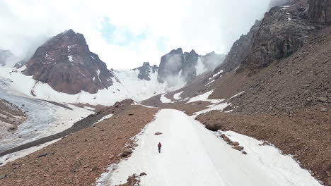 a lone hiker walks through a vast snowy mountain valley surrounded by rugged peaks