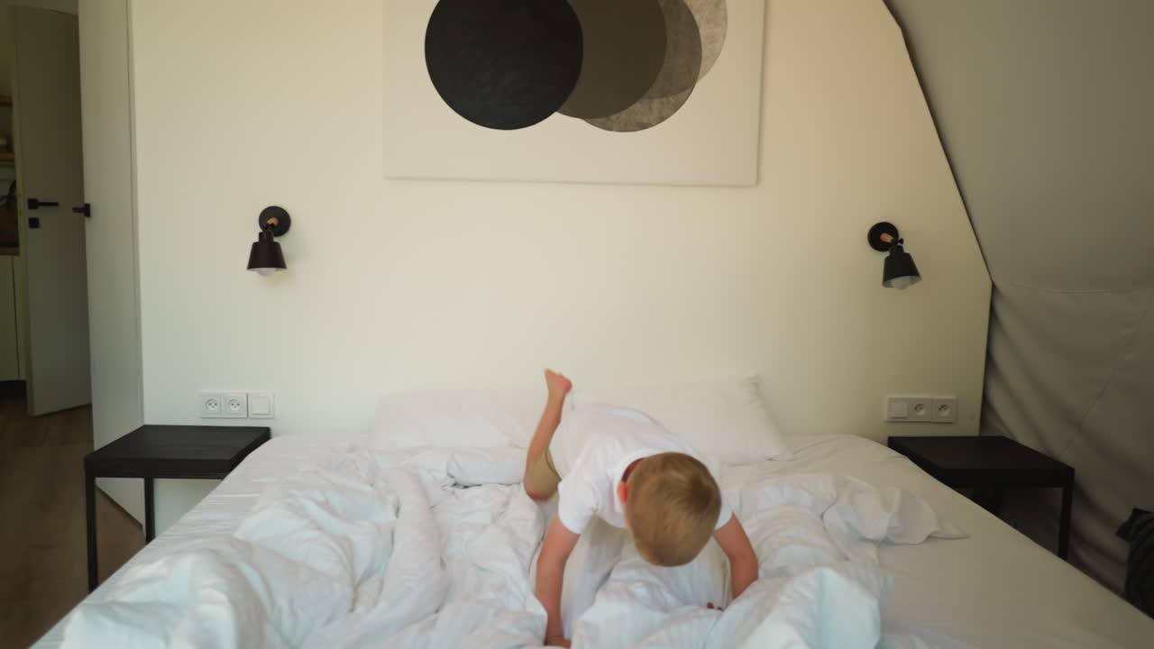 아이가 글램핑에서 담요와 함께 침대에 뛰어들고, 사랑스러운 어린 소년은 텐트 호텔 침실에서 부드러운 플레이드에 떨어집니다. 활동적인 아이는 캠핑에서 재미있습니다.