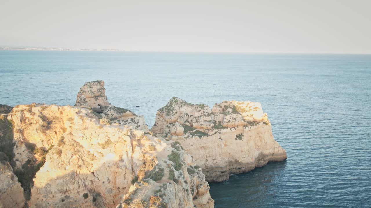 Camera spirals around natural stone archways and golden cliffs, highlighting aquamarine waters and revealing layers of Portugal’s iconic shoreline