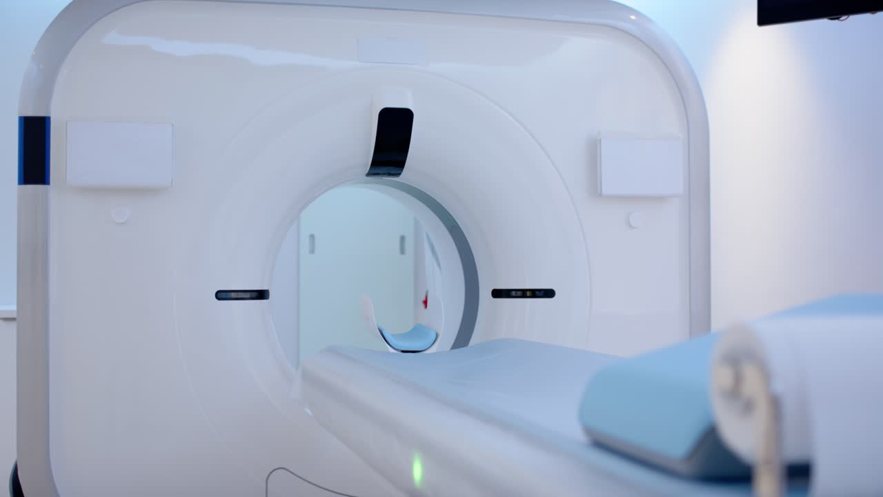 La telecamera si allontana e si alza, rivelando il gantry dello scanner con il tavolo che si allinea per la scansione in una sala TC.