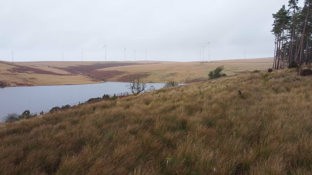 antena lateral del embalse con turbina eólica en el fondo de la colina rural - disparo de drones 4k