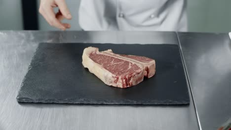 Chef-preparing-to-cook-at-kitchen-restaurant.-Closeup-chef-hands-with-raw-steak.