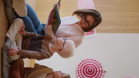 Vertical-video-of-a-woman-with-a-bob-hairstyle-in-glasses-in-a-pink-shirt-reading-a-green-book-for-her-students-of-preschool-children-in-a-club-for-preparing-children-for-school