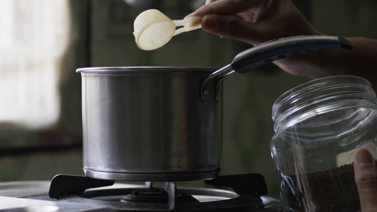 A close-up, slow-motion of a hand putting tea from a glass jar with a scoop into a pot on the stove. Tea preparation