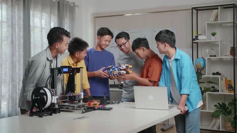 asian man with a laptop and 3d printing teaching the boys assembling a cyborg hand at school