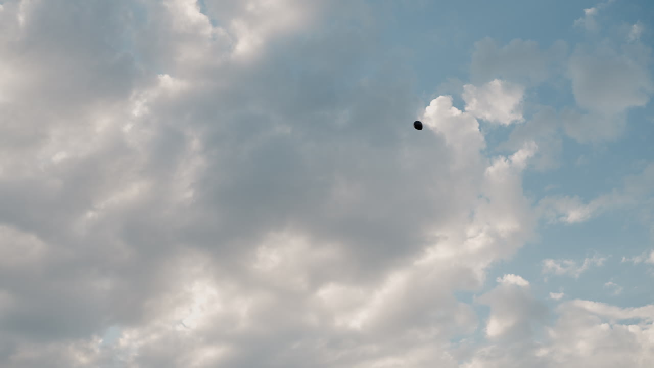 black balloon drifts across cloudy sky at sunset while researchers release and track device from field creating mood of exploration and discovery in natural landscape with atmospheric lighting