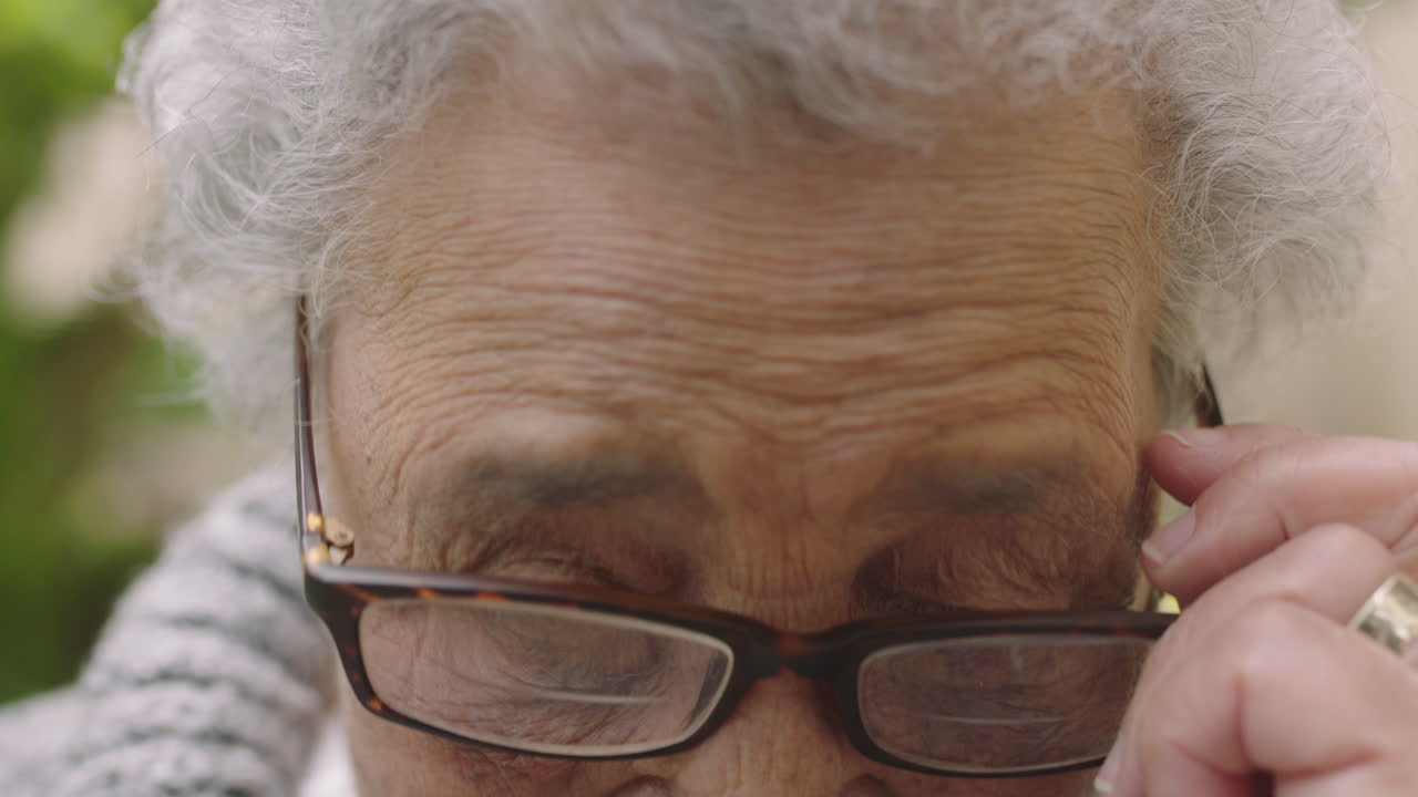 retrato de una anciana frágil con los ojos cansados mirando a la cámara sonriendo poniéndose gafas