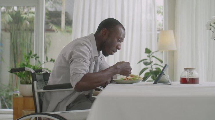 Uomo in sedia a rotelle che mangia e guarda video su tablet