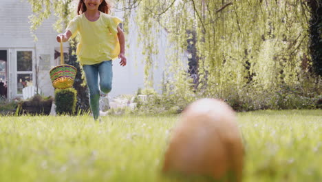 girl wearing bunny ears running to pick up chocolate egg on easter egg hunt in garden