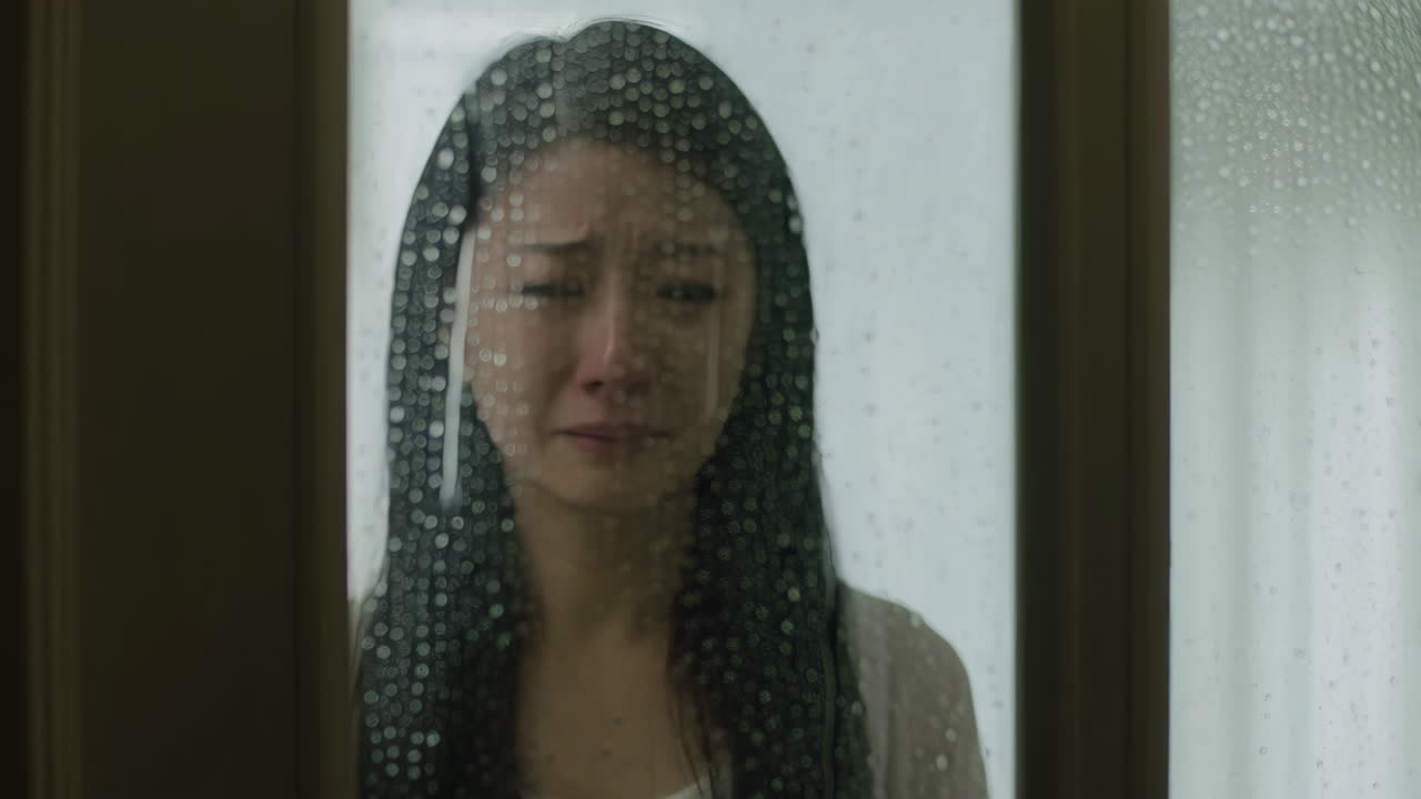 A woman crying behind a rainy window