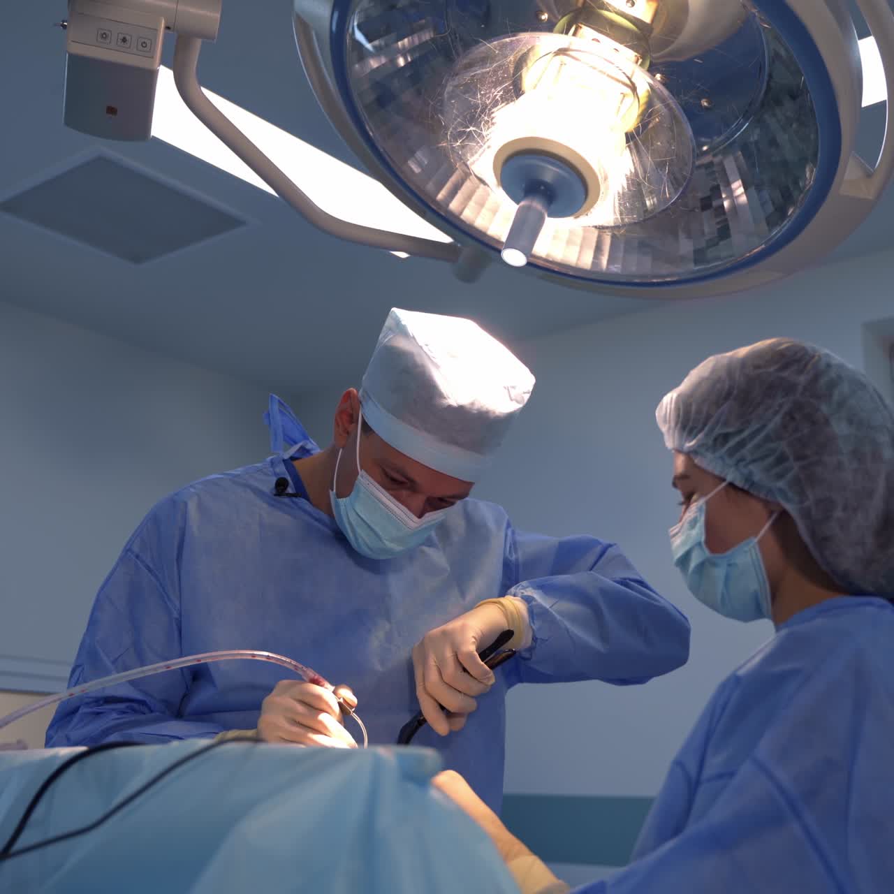 Experienced surgeon performs operation holding instruments in both hands. Assistants at backdrop in surgery room