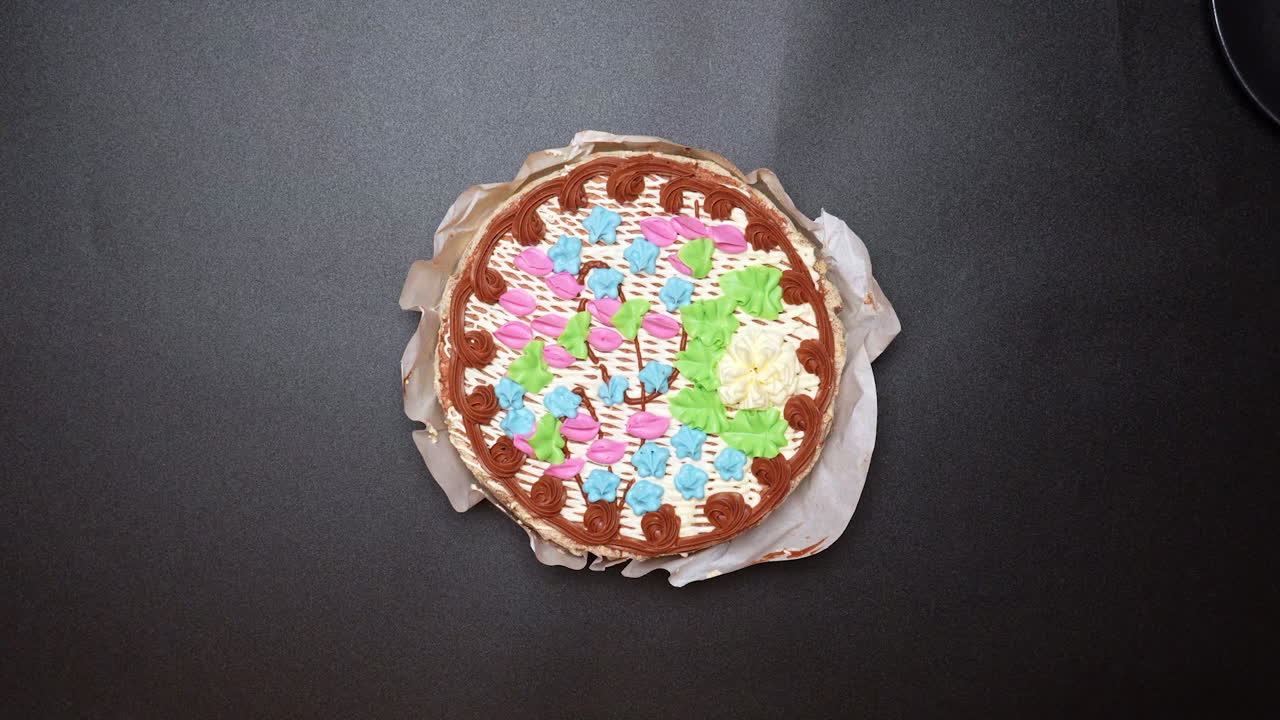 Decorating a cake with colorful icing patterns in a kitchen setting. Hands hold a decorated cake with bright icing in a kitchen. The cake has a variety of colors arranged in a pattern