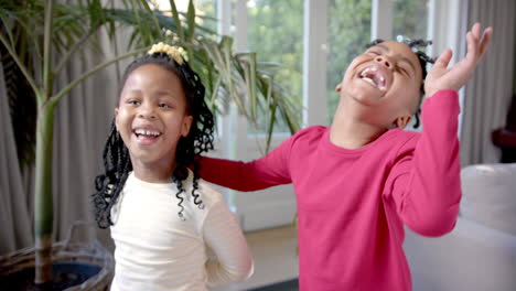 happy african american brother and sister laughing and embracing in sunny living room, slow motion