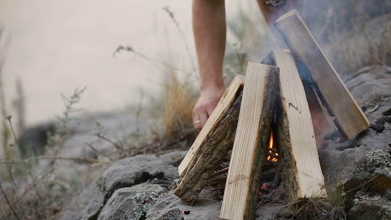 Making Fire In The Forest. Young man kindles a fire in summer wood