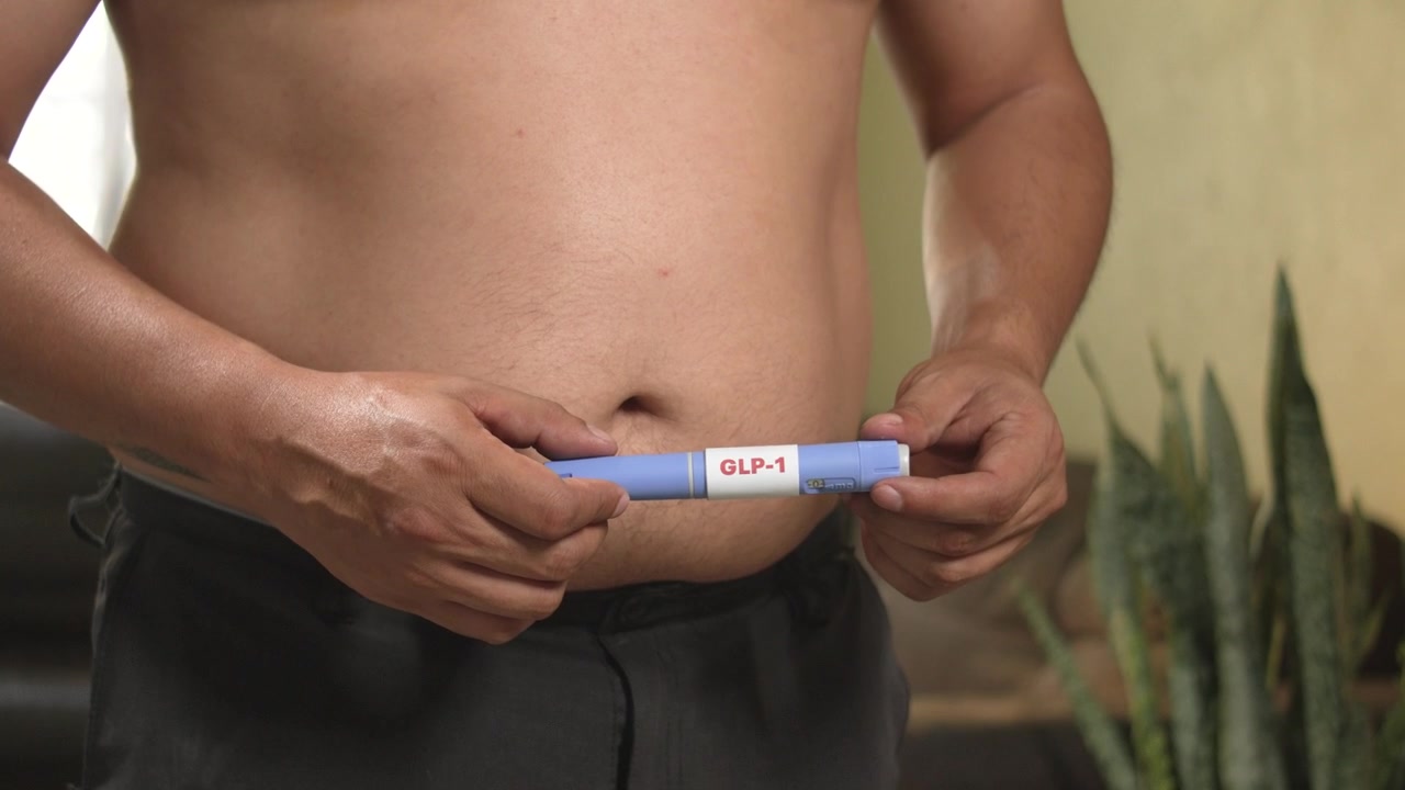 Uomo in sovrappeso che prepara una penna per farmaco GLP-1, supporto per la sindrome metabolica, innovazione sanitaria.