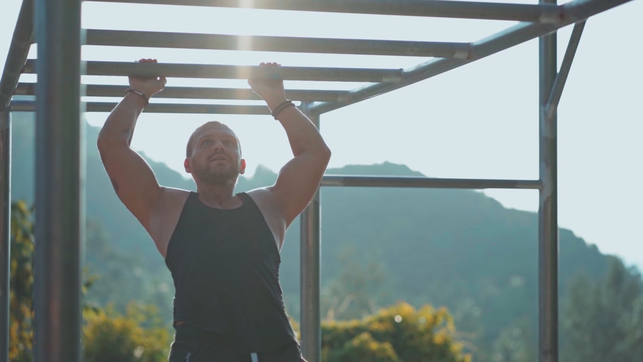 Homem musculoso fazendo barras em espaldar ao ar livre.