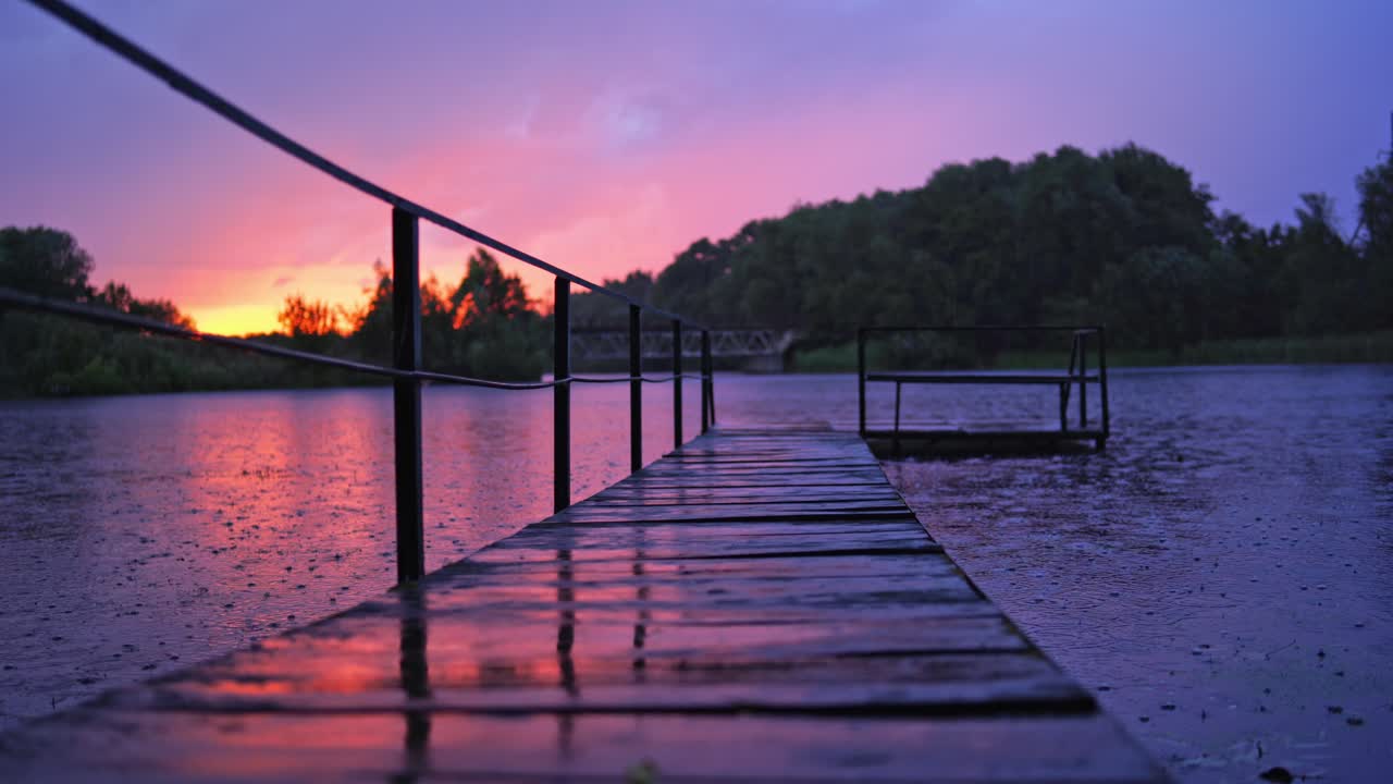 Heavy rain with small lightning over the river. Long footbridge in the river during the rain in the evening in summer. Beautiful natural background at sunset with rainy drops outdoors.