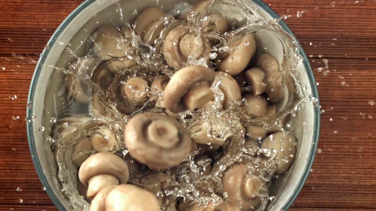 Friske sjampinjonger som plasker ned i vann i en bolle