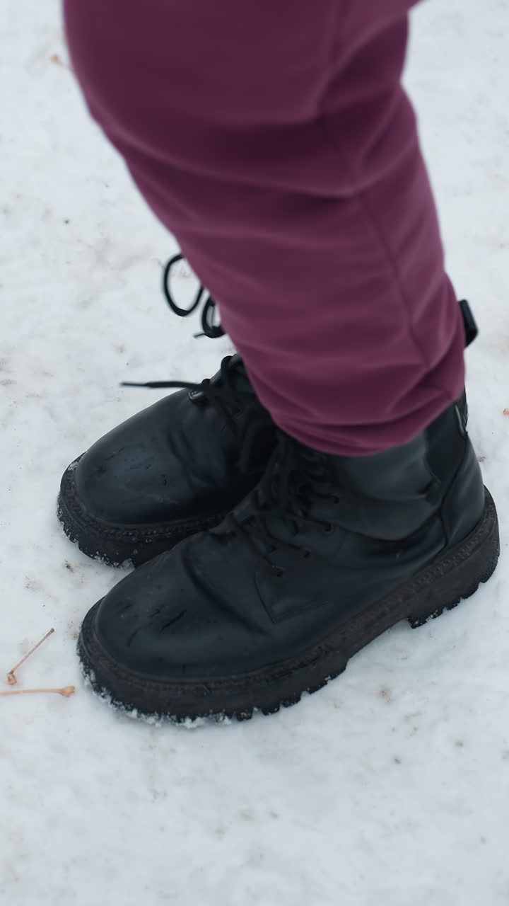 vista de ángulo inferior de arriba hacia abajo de individuos que llevan botas negras jugando activamente en un terreno cubierto de nieve con follaje seco esparcido
