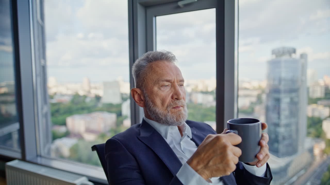Imprenditore intelligente beve caffè seduto in ufficio vicino alla finestra panoramica