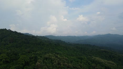 Imágenes-Aéreas-Que-Se-Deslizan-Hacia-La-Derecha-Y-Revelan-Una-Exuberante-Selva-Tropical,-Montañas-En-El-Horizonte-Y-Fantásticas-Formaciones-De-Nubes-En-El-Cielo