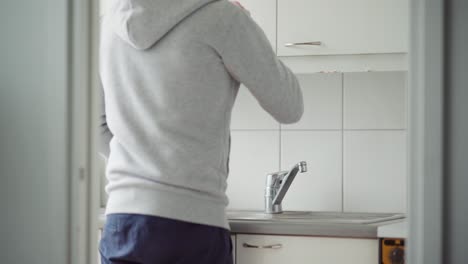 man filling up his glass with tap water and then drinking it