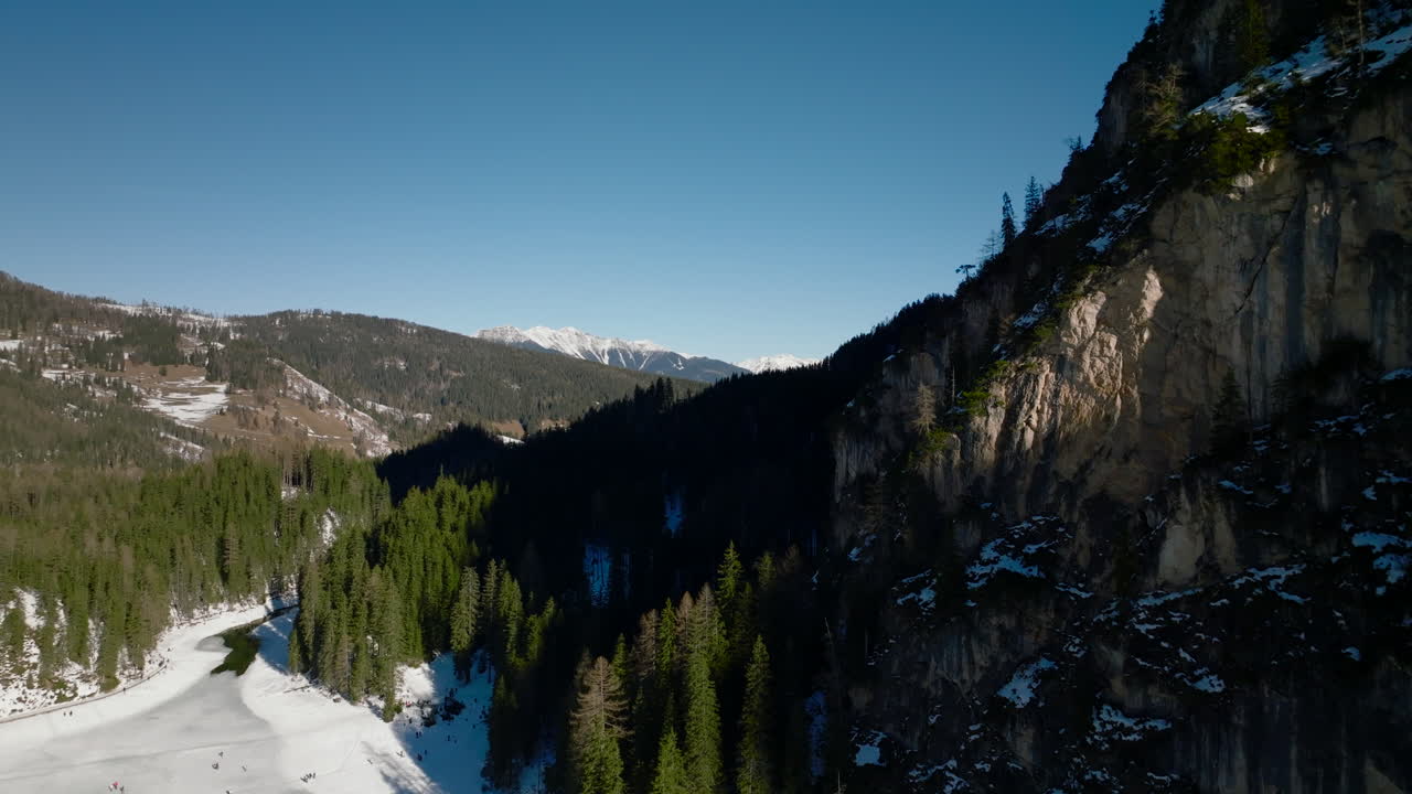 Montagne boscose in ombra vicino al Lago di Braies con carrellata all'indietro che rivela un paesaggio ghiacciato sul fondovalle
